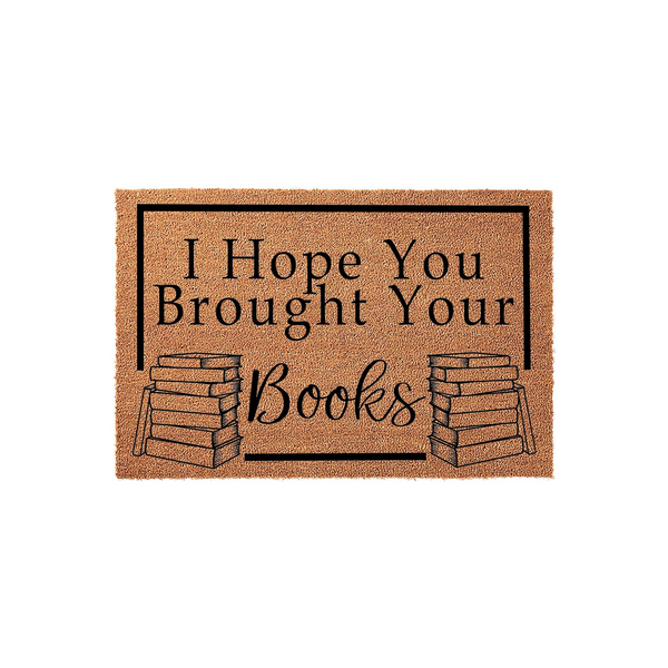 I Hope You Brought Your Books coir doormat features a natural tan fiber texture with a black rectangular border, printed with the text and illustrations of two stacks of books on a plain white background for a modern home