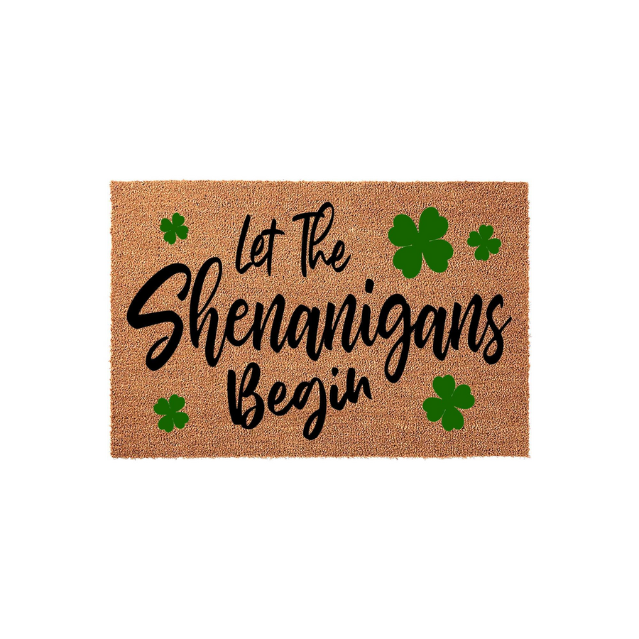 St. Patrick's Day coir doormat featuring the text Let The Shenanigans Begin in black script and block lettering, accented with several vibrant green shamrock clovers on a natural tan fiber background for a festive entryway decor.