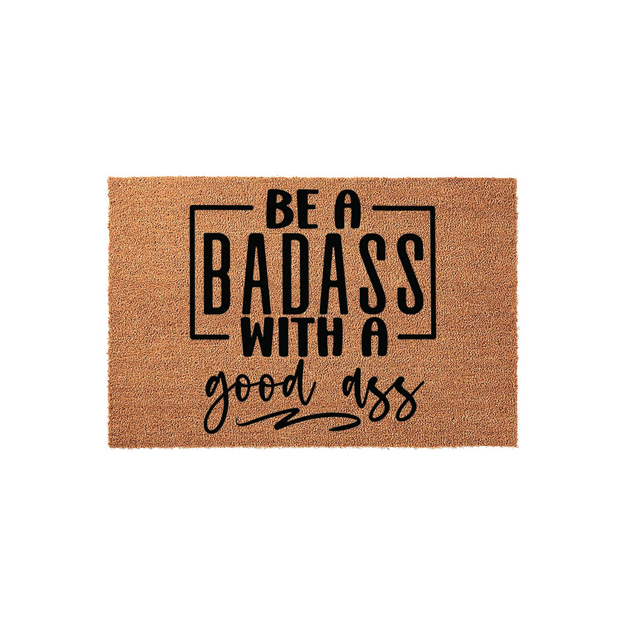 Funny Badass Doormat featuring bold black typography on a natural coir fiber background, displaying the humorous quote Be a Badass with a good ass in a mix of modern block and script fonts for a stylish and welcoming home