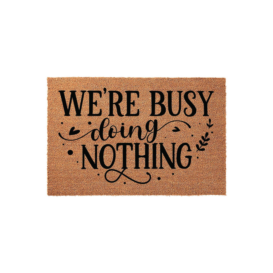 We're Busy Doing Nothing funny coir doormat featuring bold black typography on a natural tan fiber background, creating a humorous and welcoming entrance decor piece for your front porch or home entryway that adds a touch of
