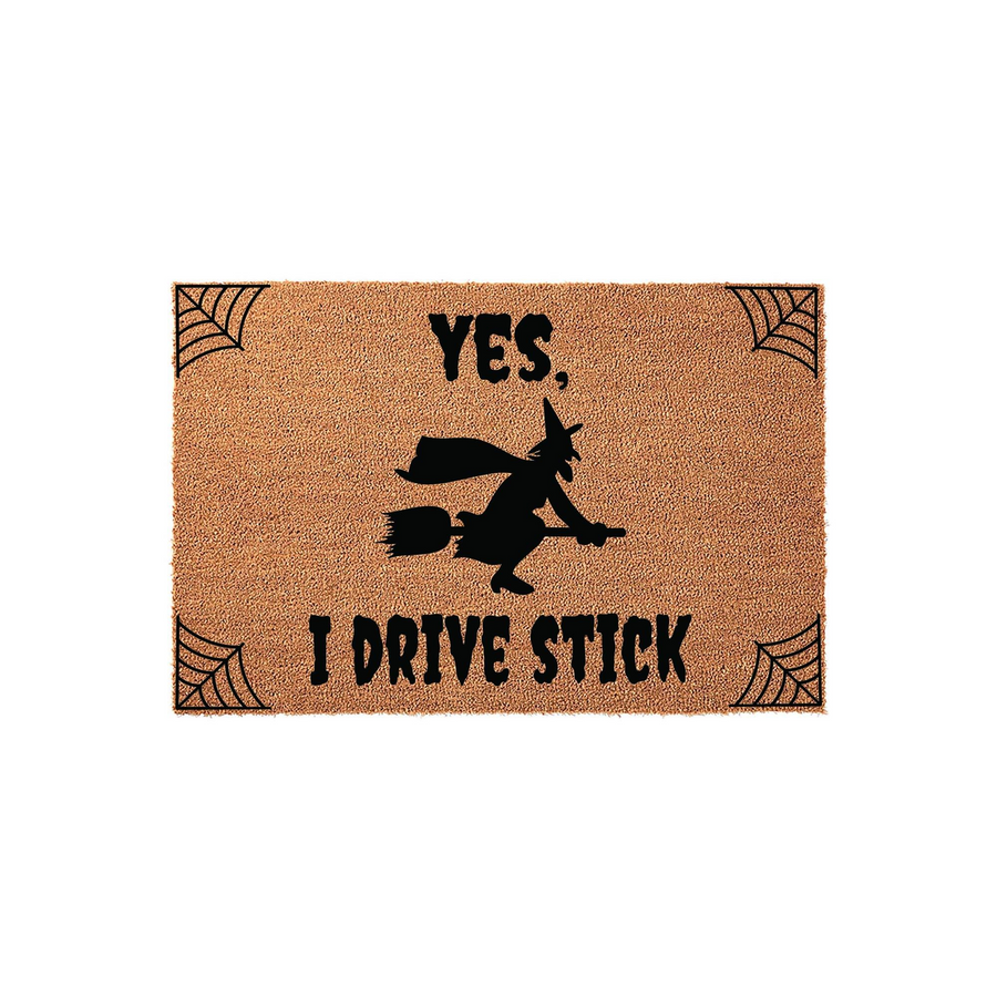 Funny Halloween witch doormat featuring a silhouette of a witch flying on a broomstick with the text Yes, I Drive Stick, accented by spider web corner designs on a natural coir fiber background for a festive seasonal entryway