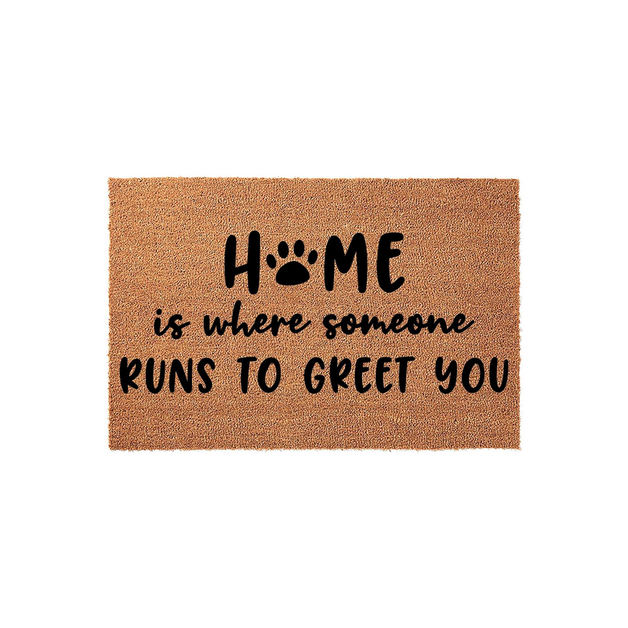 Dog lover coir doormat featuring the text Home is where someone runs to greet you with a black paw print replacing the letter O, set against a plain white background to highlight the natural fiber texture of this pet themed