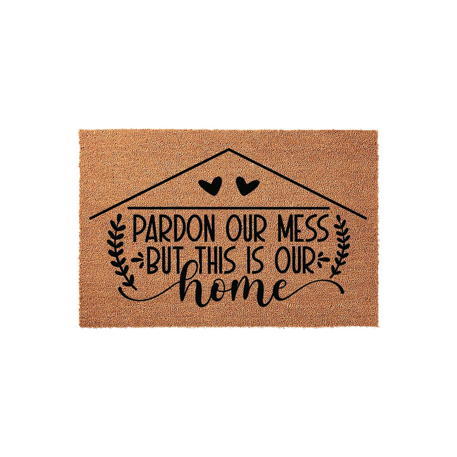 Pardon Our Mess But This Is Our Home coir doormat featuring a black house outline with two hearts and leafy branch accents, providing a welcoming and humorous touch to your front porch entryway decor on a natural fiber background.