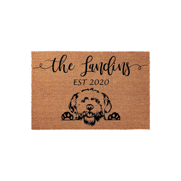 Personalized Goldendoodle doormat featuring a cute illustrated dog peeking over the bottom edge, printed on a natural coir fiber mat with a custom family name and established year in elegant black script lettering for a welcoming