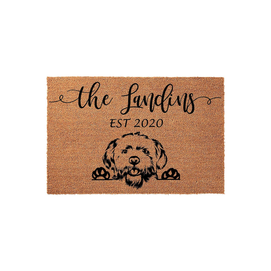 Personalized Goldendoodle doormat featuring a cute illustrated dog peeking over the bottom edge, printed on a natural coir fiber mat with a custom family name and established year in elegant black script lettering for a welcoming