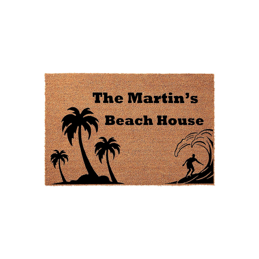 Personalized Beach House Coir Doormat featuring a tropical palm tree and surfer silhouette design, with custom text reading The Martin's Beach House printed in bold black lettering on a natural tan fiber background for a coastal