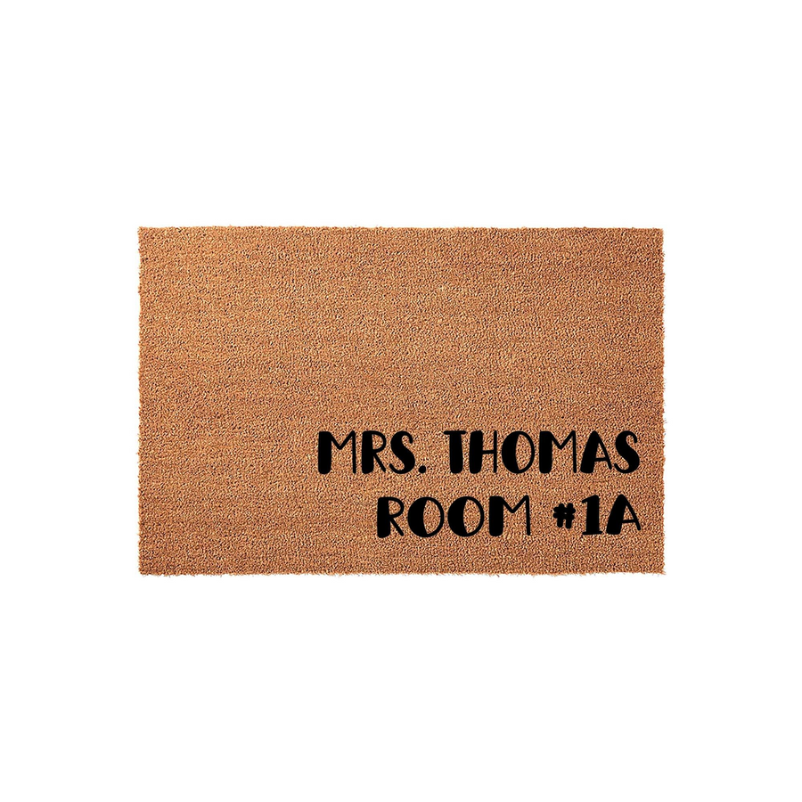 Personalized natural coir doormat featuring bold black text that reads Mrs. Thomas Room 1A, displayed against a clean white background to highlight the durable fiber texture and custom lettering for a home or classroom entrance.