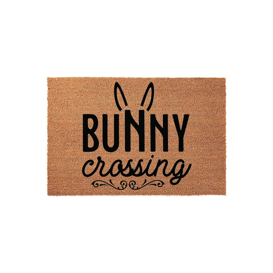 Bunny Crossing coir doormat featuring a natural tan fiber texture with black printed text and cute rabbit ears, making a festive spring or Easter front porch decor piece for your home entrance on a clean white background.