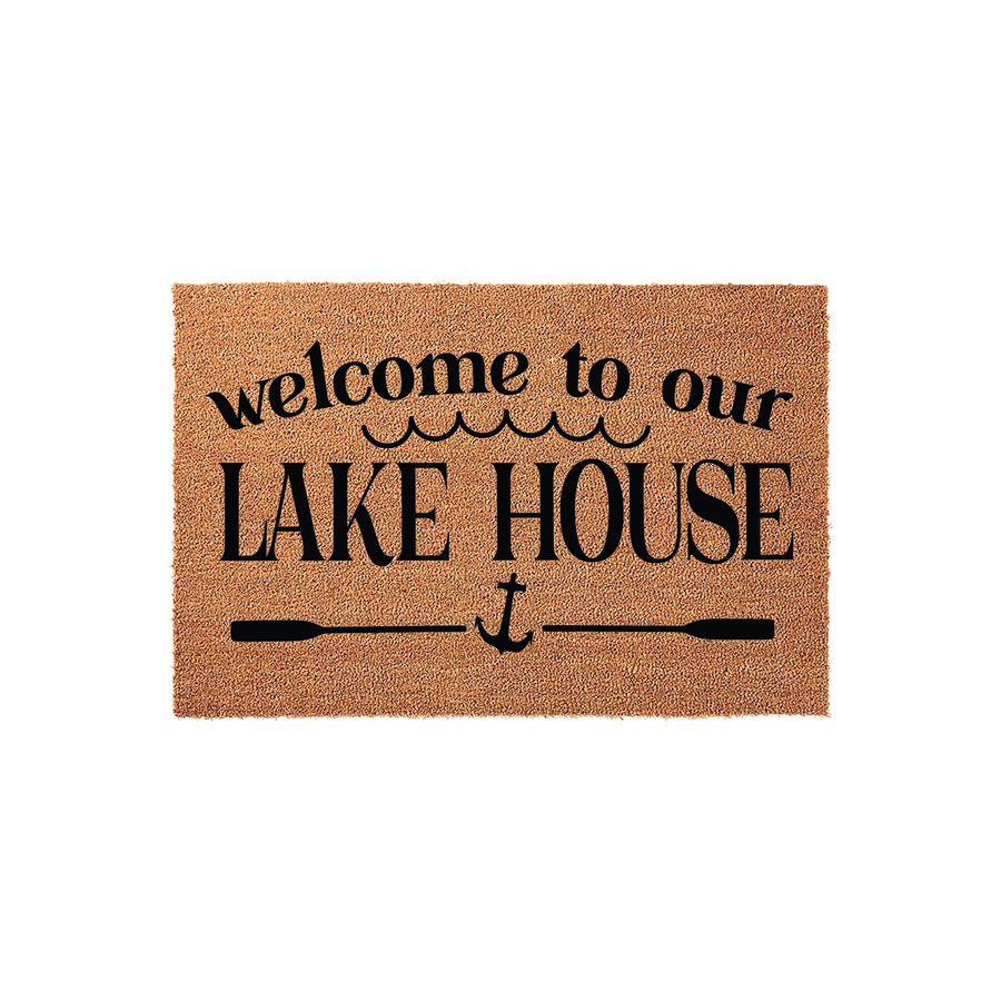 Welcome to our Lake House coir doormat featuring a natural tan fiber texture with black printed text, wavy water lines, and a nautical anchor icon centered between two horizontal oars on a clean white studio background.