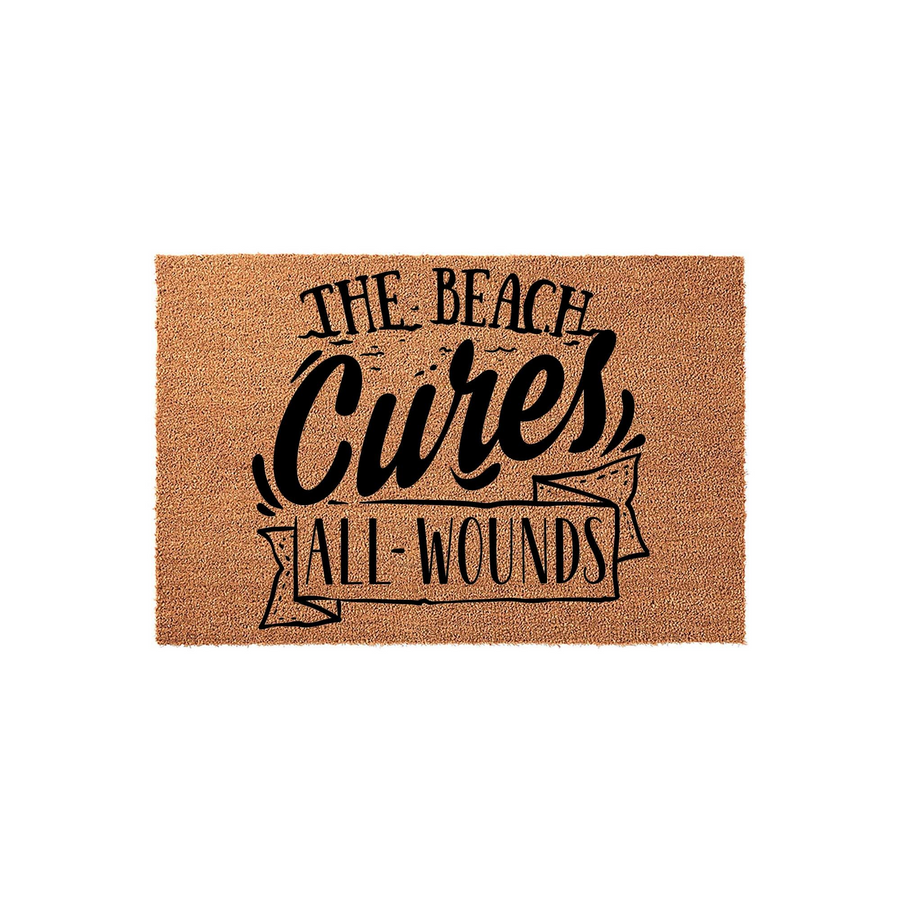 The Beach Cures All Wounds coir doormat features a natural tan fiber texture with bold black typography printed in the center, creating a coastal and relaxing entryway accent for any home that loves the ocean and summer vibes.