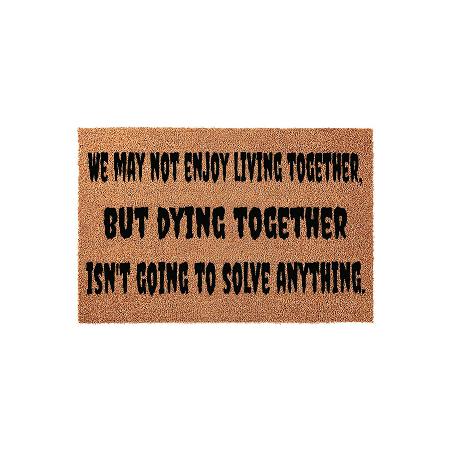 Funny Humor Doormat featuring the text We may not enjoy living together, but dying together isn't going to solve anything, printed in bold black lettering on a natural brown coir fiber mat against a clean white studio background.