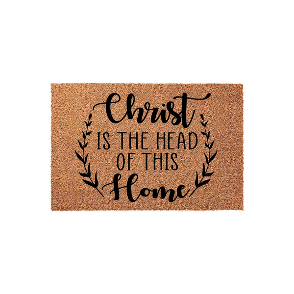 Christ Is The Head Of This Home coir doormat featuring a natural brown fiber texture and black printed text surrounded by a delicate leafy wreath design, creating a welcoming religious entryway decor piece for your front porch.