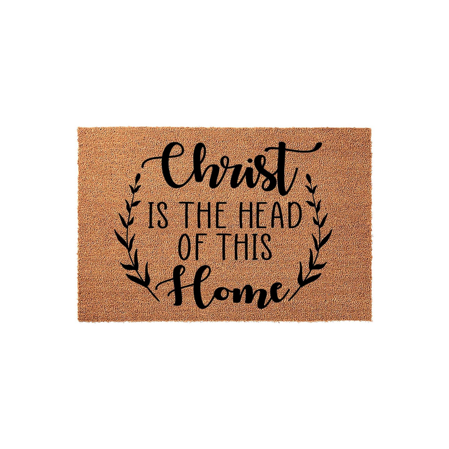 Christ Is The Head Of This Home coir doormat featuring a natural brown fiber texture and black printed text surrounded by a delicate leafy wreath design, creating a welcoming religious entryway decor piece for your front porch.
