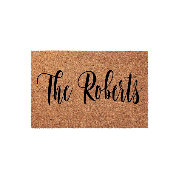 Personalized family name coir doormat featuring elegant black script lettering on a natural brown coconut fiber background, providing a welcoming and durable entrance decor piece for any home front porch or entryway floor.
