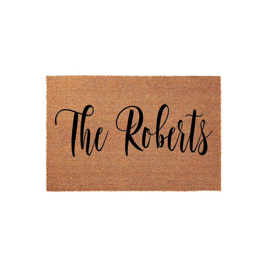 Personalized family name coir doormat featuring elegant black script lettering on a natural brown coconut fiber background, providing a welcoming and durable entrance decor piece for any home front porch or entryway floor.