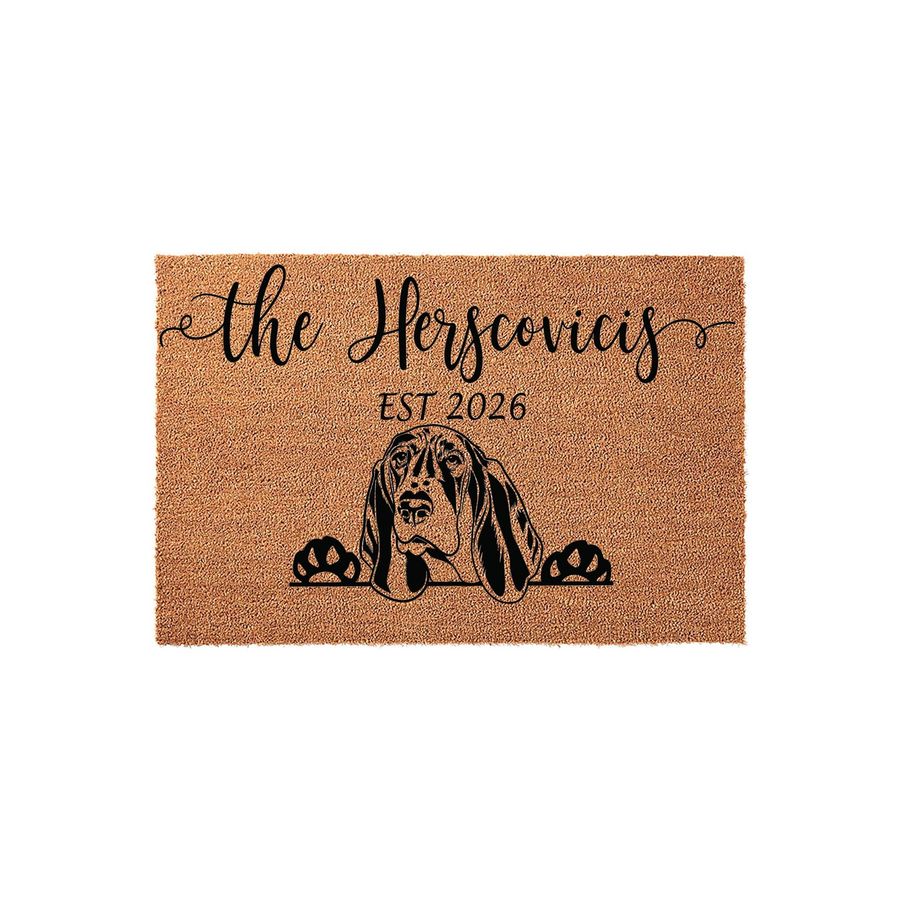 Personalized Basset Hound doormat featuring a cute dog illustration peeking over the bottom edge, customized with a family name and established year on a natural tan coir fiber background for a welcoming front porch entrance.