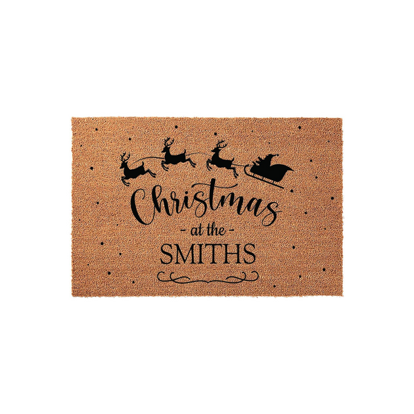 Personalized Christmas coir doormat featuring a black silhouette of Santa and his reindeer flying across the top, with the festive text Christmas at the Smiths printed in the center against a natural brown textured fiber