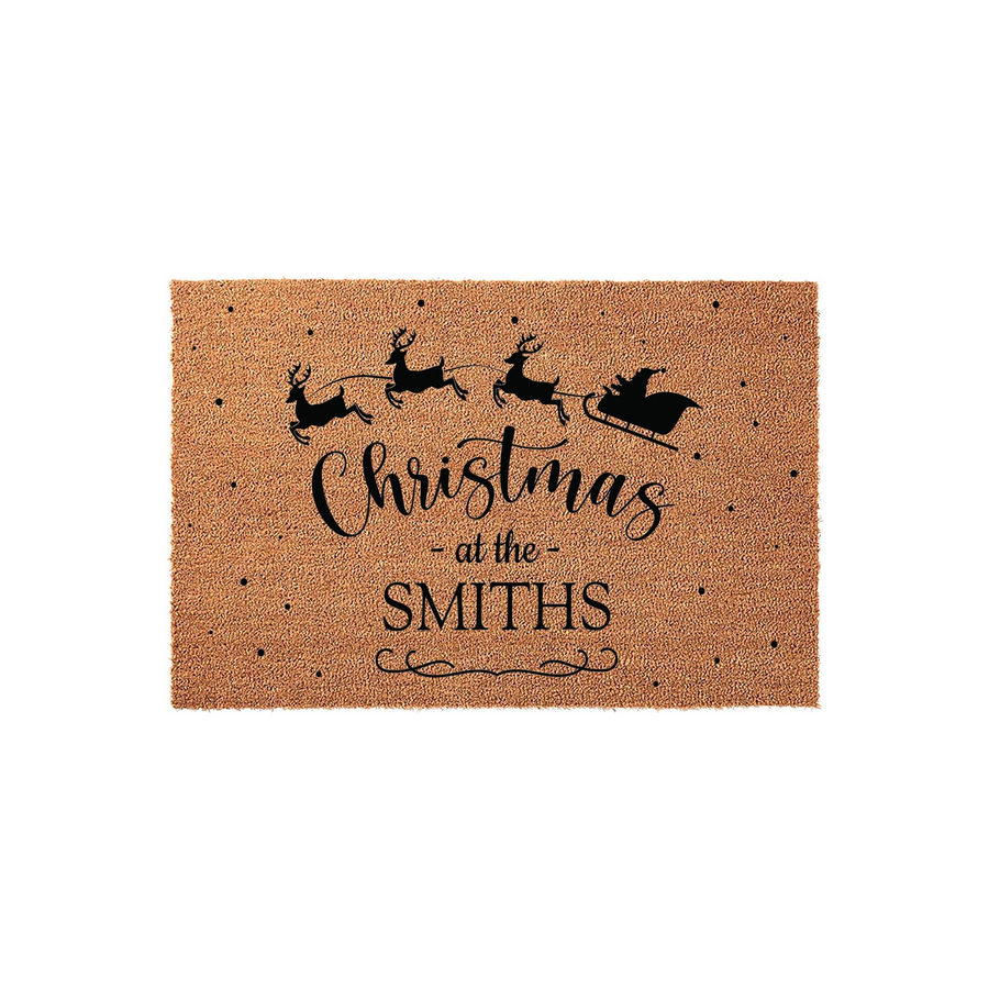 Personalized Christmas coir doormat featuring a black silhouette of Santa and his reindeer flying across the top, with the festive text Christmas at the Smiths printed in the center against a natural brown textured fiber