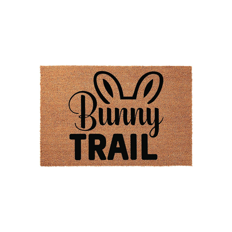 Bunny Trail Easter doormat made of natural coir fiber, featuring black printed text and cute rabbit ears on a rectangular mat, providing a festive and welcoming touch to your front porch decor for the spring holiday season.