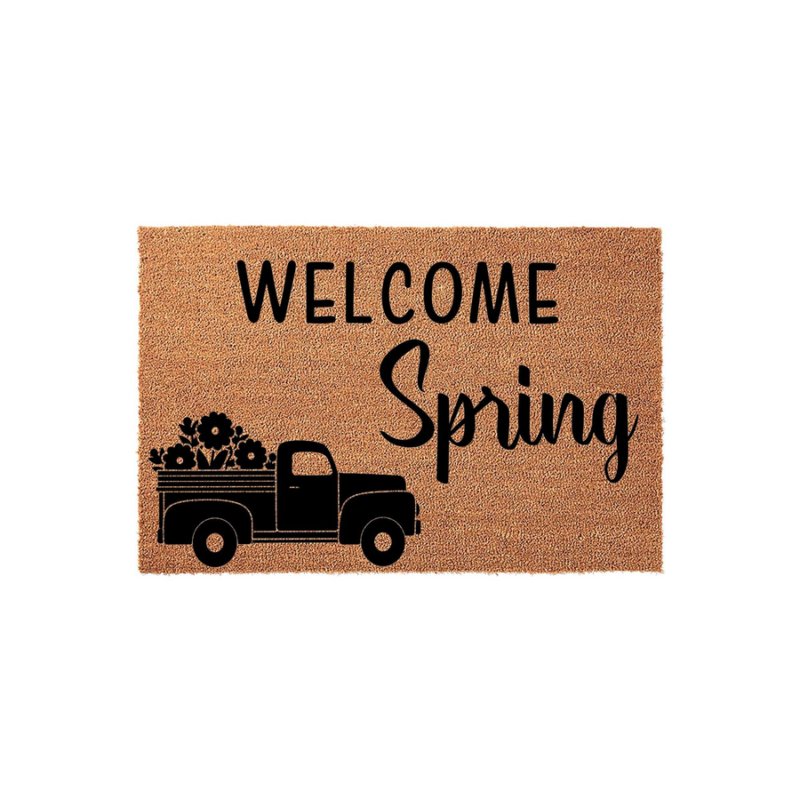 Spring Welcome Doormat featuring a rustic truck carrying a bed full of flowers, printed in black ink on a natural tan coir fiber mat, creating a seasonal entryway decor piece for your front porch or home entrance during the