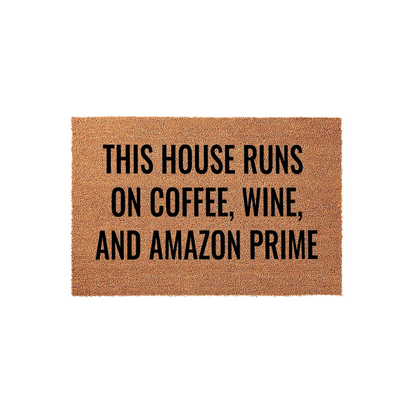 Funny Coffee and Wine Doormat featuring the text This House Runs On Coffee, Wine, And Amazon Prime in bold black lettering on a natural tan coir fiber background, perfect for a humorous front porch welcome mat for any modern home.