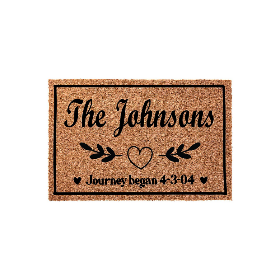 Personalized family name coir doormat featuring a rustic brown texture with black script text that reads The Johnsons and Journey began, accented by a central heart and leaf design on a clean white background for a custom home