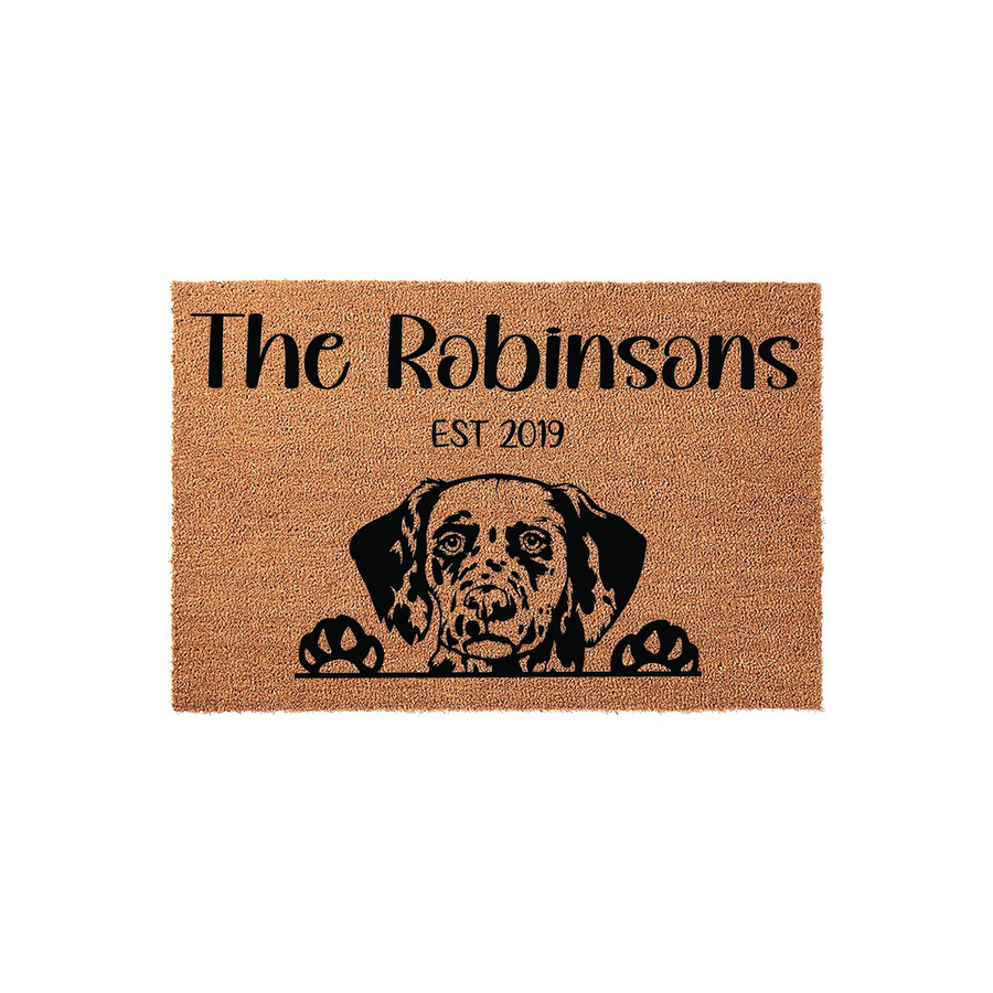 Personalized Dalmatian doormat featuring a cute dog peeking over the bottom edge, printed on a natural coir fiber mat with a custom family name and established year in elegant black lettering against the textured brown background.