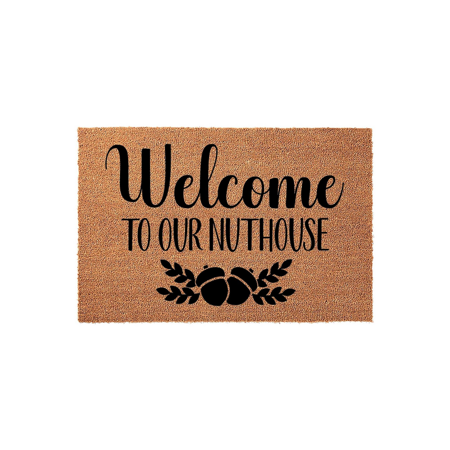 Welcome to Our Nuthouse coir doormat featuring a natural brown fiber texture with black printed text and a decorative acorn illustration, providing a humorous and rustic entryway accent for your front porch or home entrance decor.