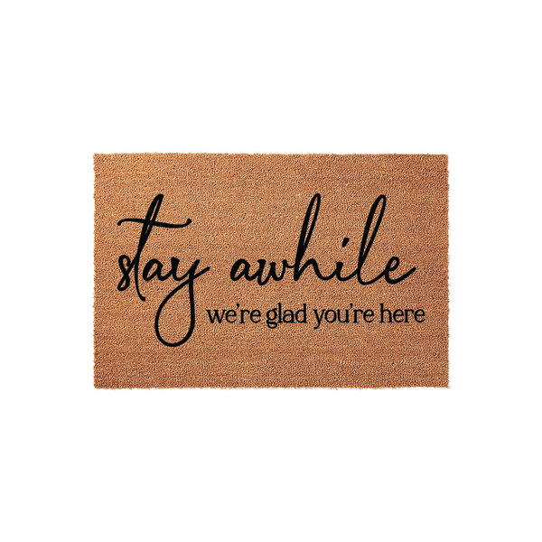 Stay Awhile We Are Glad You Are Here Coir Doormat featuring a natural tan fiber texture with black script and serif lettering, creating a welcoming front porch entrance for guests arriving at your home on a clean white background.