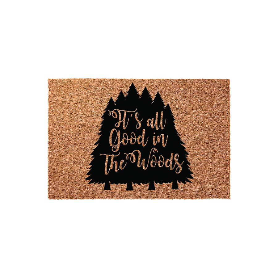 It's All Good in the Woods natural coir doormat featuring a black silhouette of pine trees and rustic cursive lettering, providing a charming outdoor welcome mat for your cabin, lodge, or woodland-themed home entryway decor.