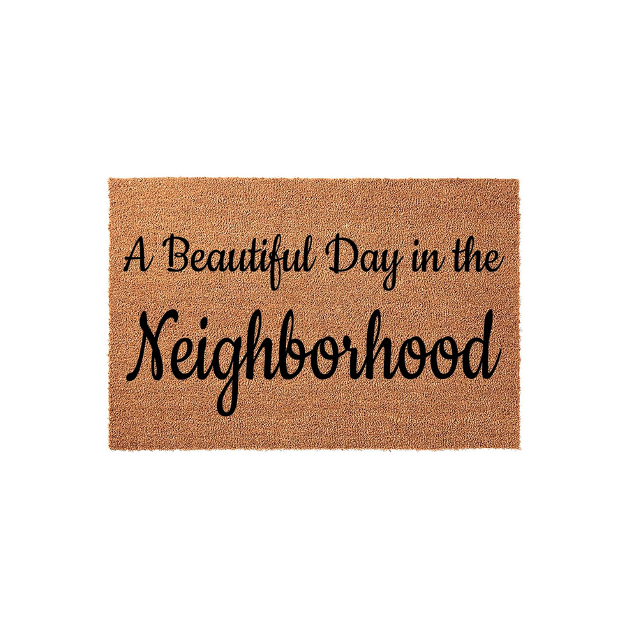 A Beautiful Day in the Neighborhood coir doormat featuring natural brown coconut fibers and bold black script lettering, providing a welcoming and friendly entrance decor piece for your front porch or home entryway on a plain