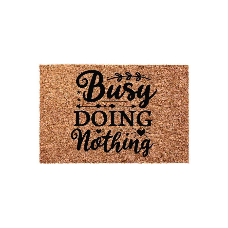 Busy Doing Nothing coir doormat featuring a natural brown fiber texture and bold black typography, centered on a plain white background to highlight the humorous message and decorative arrow and heart accents for a front porch