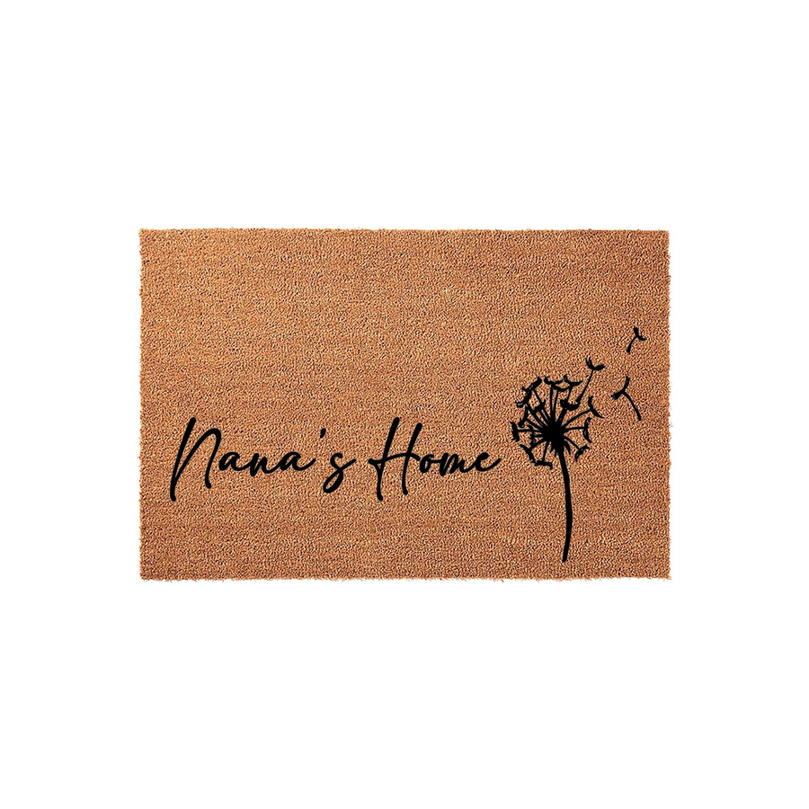 Nana's Home coir doormat featuring a natural tan fiber texture and black script lettering, accented by a delicate dandelion design with seeds blowing in the wind, set against a clean white background for a simple entryway