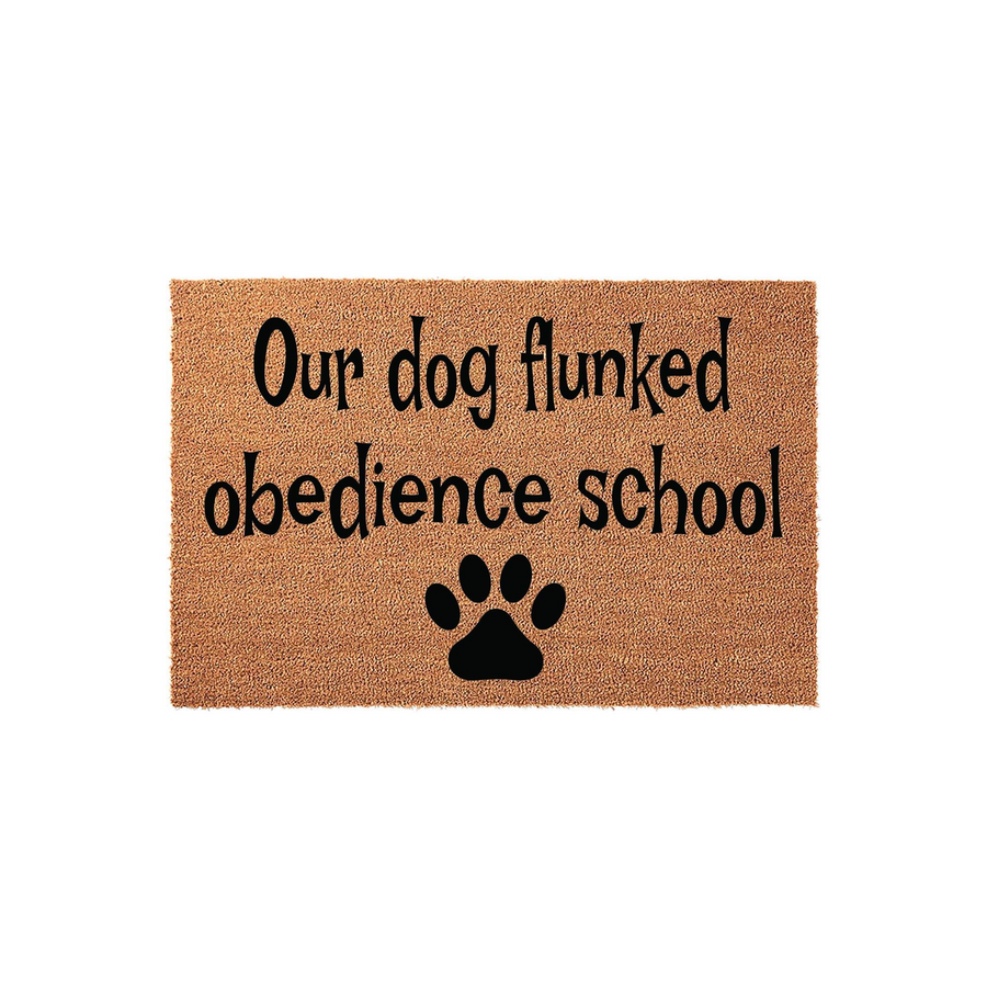 Funny Dog Lover Doormat featuring the text Our dog flunked obedience school in black lettering on a natural tan coir fiber background, complete with a single black paw print icon centered at the bottom of this rectangular