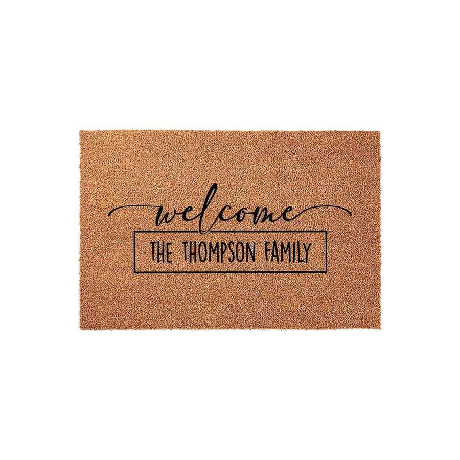 Personalized family name welcome doormat featuring a natural coir texture with black script lettering that says welcome above a rectangular box containing custom text, creating a classic farmhouse aesthetic for your front porch