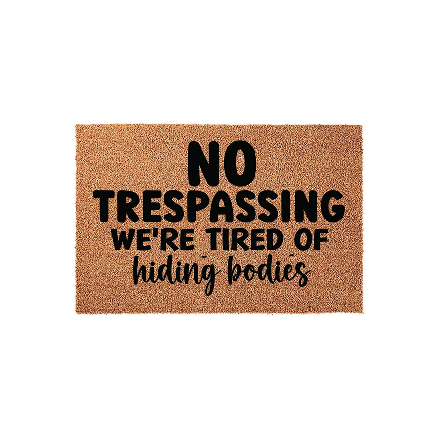 Funny No Trespassing doormat made of natural coir fiber, featuring bold black text that reads No Trespassing We're Tired of Hiding Bodies, perfect for a humorous front porch entrance or a unique housewarming gift for a dark humor