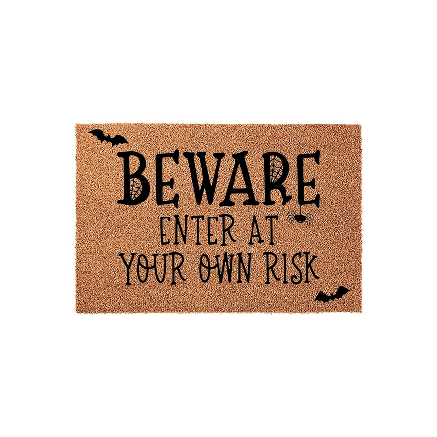 Beware Enter At Your Own Risk Halloween doormat made of natural coir fiber, featuring black printed text, a hanging spider, and flying bat silhouettes against a plain white background for a spooky seasonal entryway decoration.