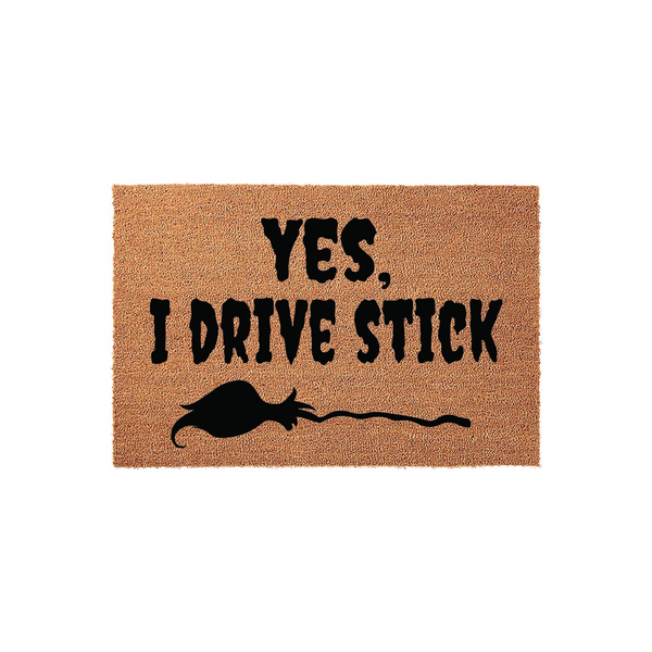 Yes I Drive Stick funny doormat made of natural coir fiber, featuring bold black text and a silhouette of a witch flying on a broomstick, perfect for a whimsical front porch entrance that showcases a love for Halloween and