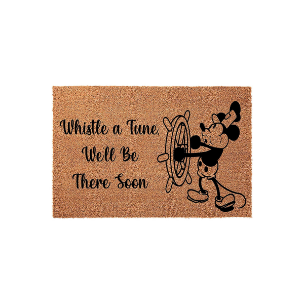 Mickey Mouse nautical doormat featuring a classic cartoon character steering a ship wheel with the text Whistle a Tune, We'll Be There Soon printed in black on a natural brown coir fiber background for a fun entryway decor accent.
