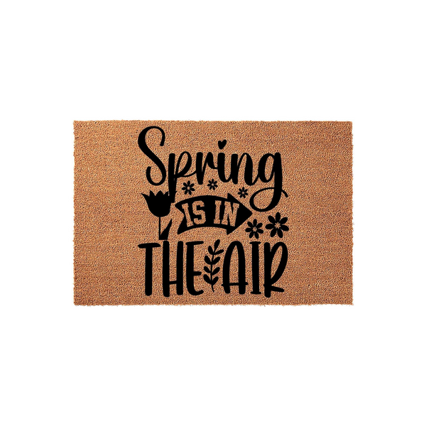 Spring Is In The Air coir doormat featuring a natural brown fiber texture and bold black lettering with decorative floral accents, creating a cheerful seasonal welcome for your front porch entryway during the spring season.