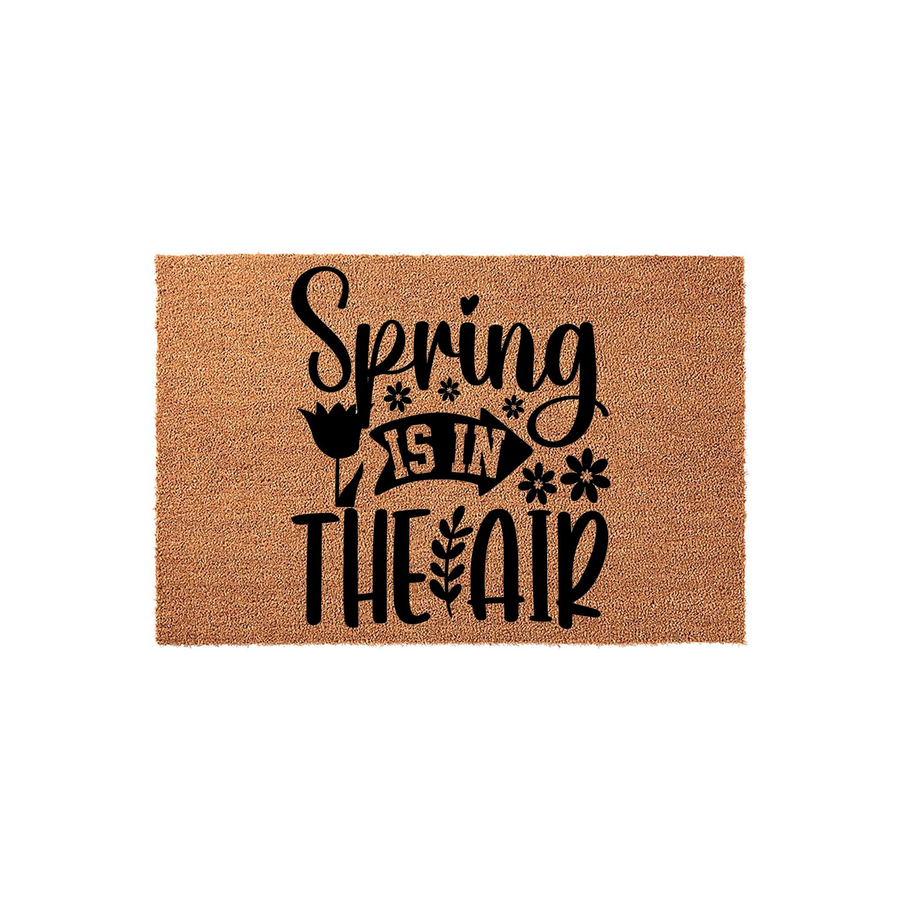 Spring Is In The Air coir doormat featuring a natural brown fiber texture and bold black lettering with decorative floral accents, creating a cheerful seasonal welcome for your front porch entryway during the spring season.