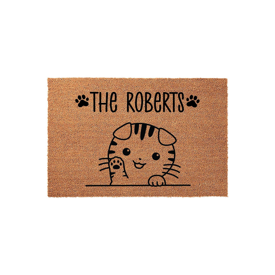 Personalized cat family doormat featuring a cute illustrated tabby kitten waving from behind a line, with space for a custom family name printed in black ink on a natural tan coir fiber background for a welcoming home entrance.