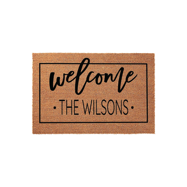 Personalized family name coir doormat featuring a black rectangular border, the word welcome in a script font, and a custom last name printed in a clean sans-serif typeface on a natural brown textured coconut fiber background.