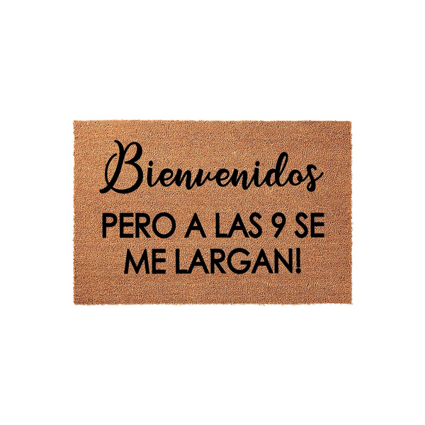 Funny Spanish welcome doormat made of natural coir fiber, featuring the text Bienvenidos pero a las 9 se me largan in a mix of elegant script and bold block lettering against a plain white studio background for a humorous home