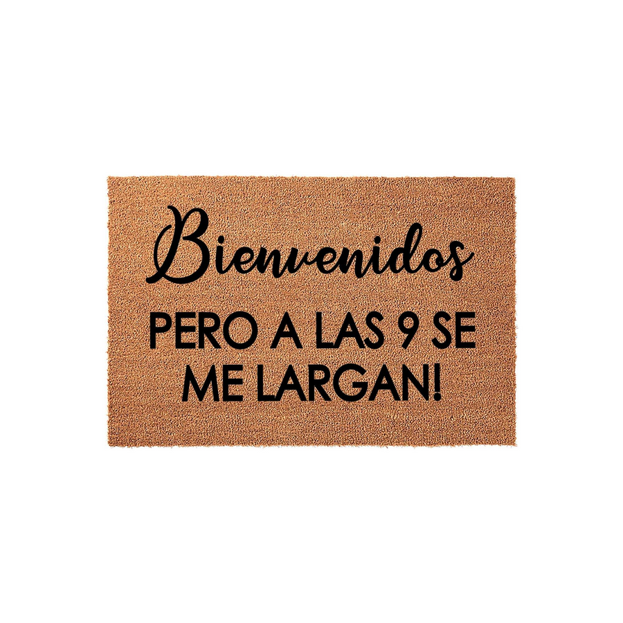 Funny Spanish welcome doormat made of natural coir fiber, featuring the text Bienvenidos pero a las 9 se me largan in a mix of elegant script and bold block lettering against a plain white studio background for a humorous home