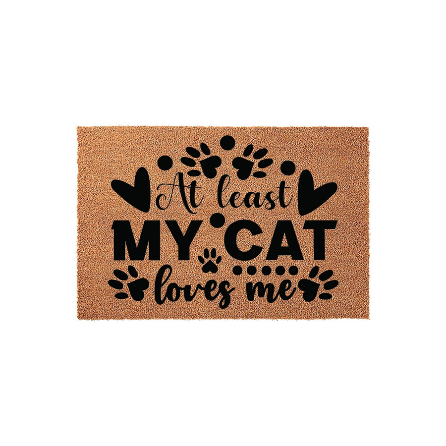 At least my cat loves me coir doormat featuring black text and paw print graphics on a natural brown fiber background, creating a humorous and welcoming entryway decor piece for any cat lover who enjoys funny home accessories.