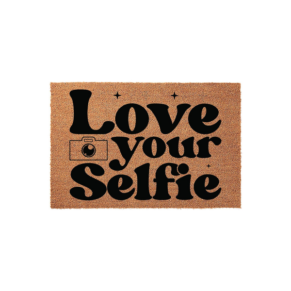 Love Your Selfie coir doormat featuring bold black typography and a camera icon on a natural brown fiber background, creating a fun and trendy entryway decor piece for your home or apartment front door that welcomes guests with