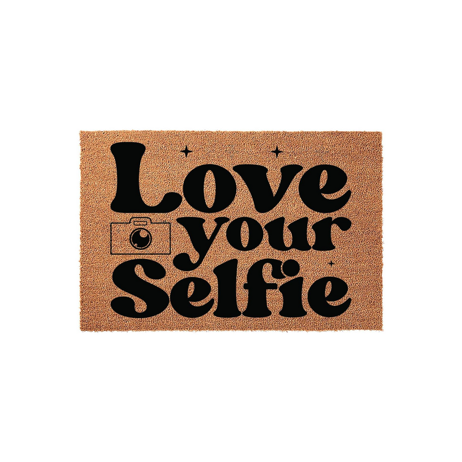 Love Your Selfie coir doormat featuring bold black typography and a camera icon on a natural brown fiber background, creating a fun and trendy entryway decor piece for your home or apartment front door that welcomes guests with