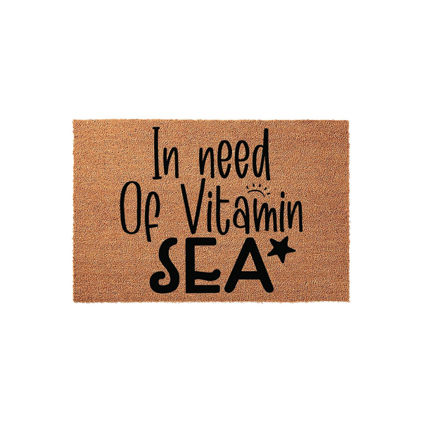 In Need Of Vitamin Sea Coir Doormat featuring a natural brown fiber texture with bold black lettering that reads In Need Of Vitamin SEA with a small sun and star icon, perfect for a beach house or coastal home entryway decor.