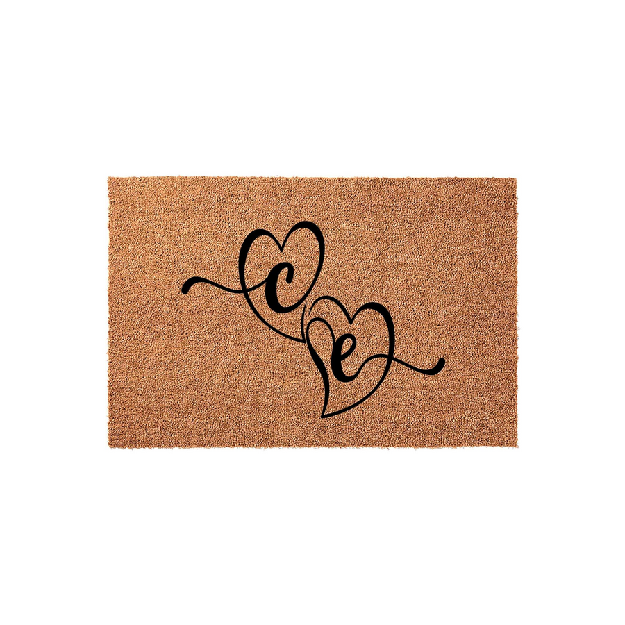 Personalized couple doormat featuring two interlocking black heart outlines with custom initials centered on a natural brown coir fiber background, creating a welcoming entryway decor piece for a new home or wedding celebration.
